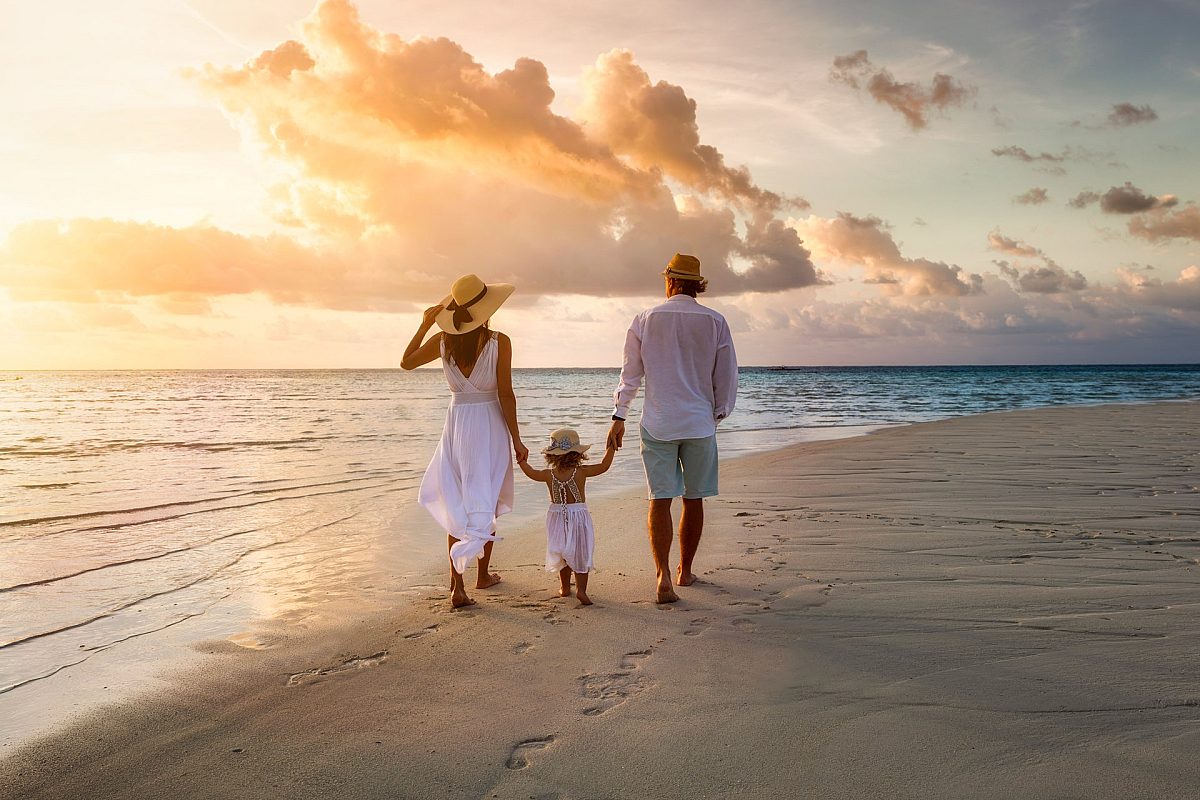 family walking on the side of the beach leaving footprints on the sand in sunset